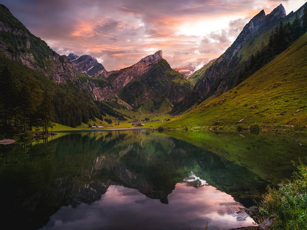 A serene Alpine lake reflecting rugged mountain peaks and a vibrant sunset, showcasing the natural beauty of Switzerland.