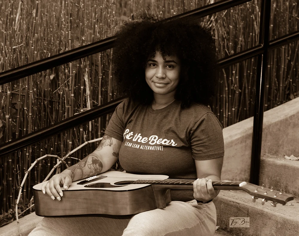 Musical Artist Posing with Acoustic Guitar Musical artist sitting on steps with an acoustic guitar, smiling confidently.