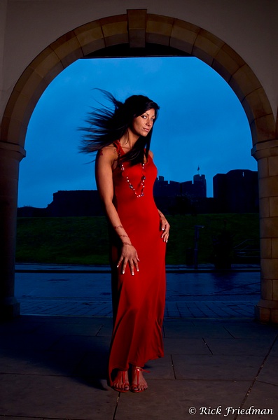 Brunette model in slinky red dress in front of castle in Whales, UK by Rick Friedman - Models - Rick Friedman Photography