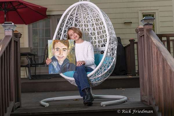 Young woman on  white swinging chair  holding a painting of her brother in RI by Rick Friedman - Rick Friedman Photography 