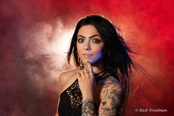 Brunette model with tattoos in front of red back drop with smoke by Rick Friedman - Models - Rick Friedman Photography