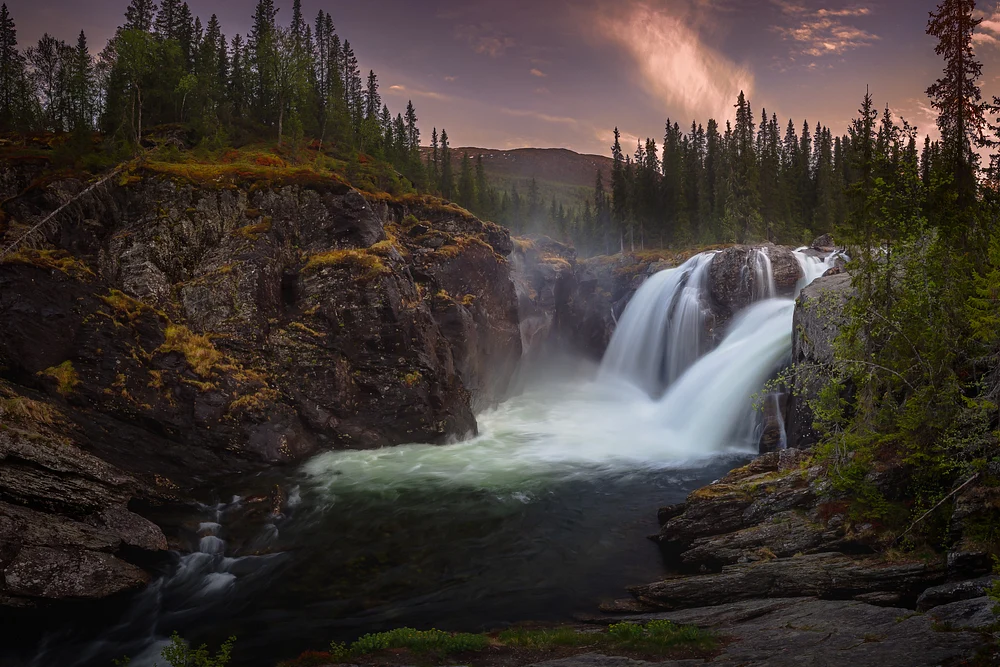 A stunning view of Rjukandefossen waterfall at midnight, surrounded by lush trees and rocky formations, capturing the serene beauty of Norway's wilderness.