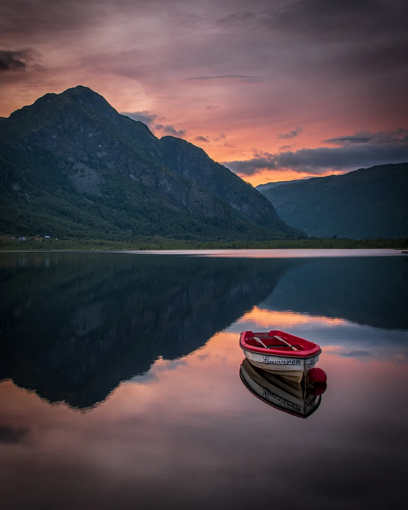 A red boat floating on the calm waters of Fagerset Lake during sunset, with mountains reflecting in the water.