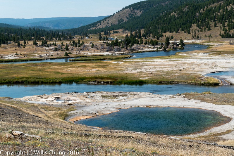 Circle pool near the Firehole River. Yellowstone National Park. West Flood Geyser across the river.