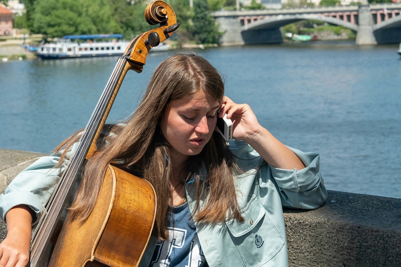 Cellist taking a call on the eastern end of the Charles Bridge, Praha, Czechia.