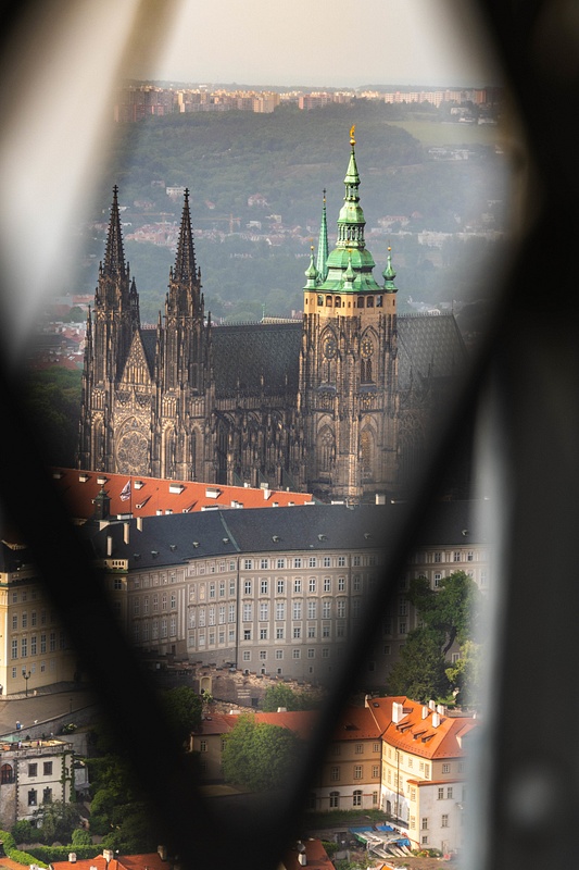 Peering through the struts of Petrin Tower at St. Vitus Cathedral .