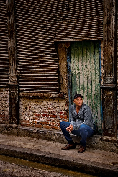 A thoughtful passenger sitting against a weathered wall in an urban setting.