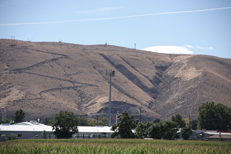 A dry, eroded hill looms over fertile, irrigated farm land.