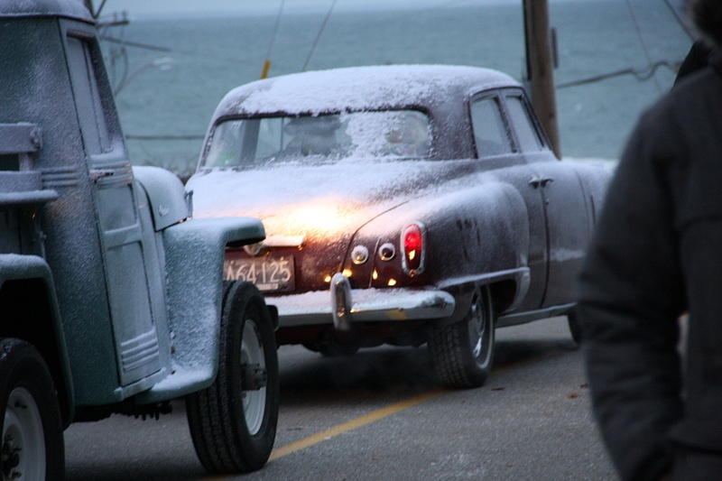 The tail end of a classic Studebaker illuminated by a vintage jeep. The 