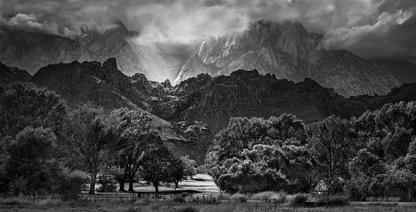 Black-and-white landscape of sunlight breaking through clouds over Lone Pine, California, with mountains and trees.