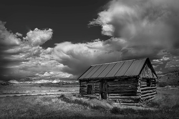 Black-and-white photograph of an abandoned cabin beneath a dramatic stormy sky in Utah.