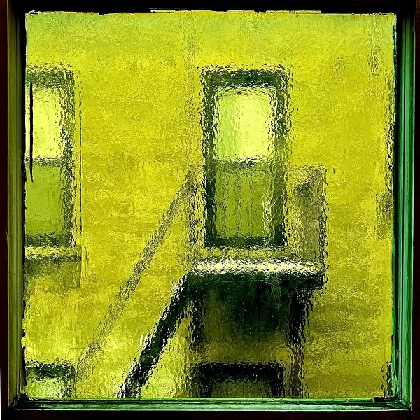 Textured chartreuse facade with dark window openings, a central ledge, and an angled shadow creating abstract depth
