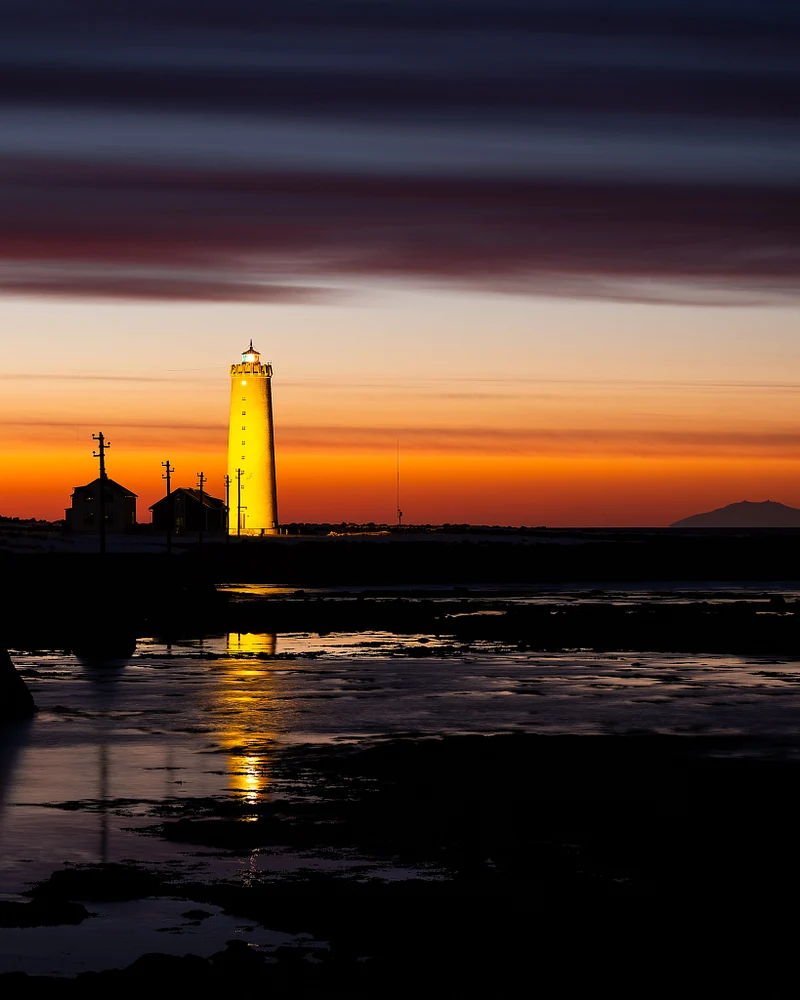 Reykjavik lighthouse glowing at sunset with colorful sky reflections.