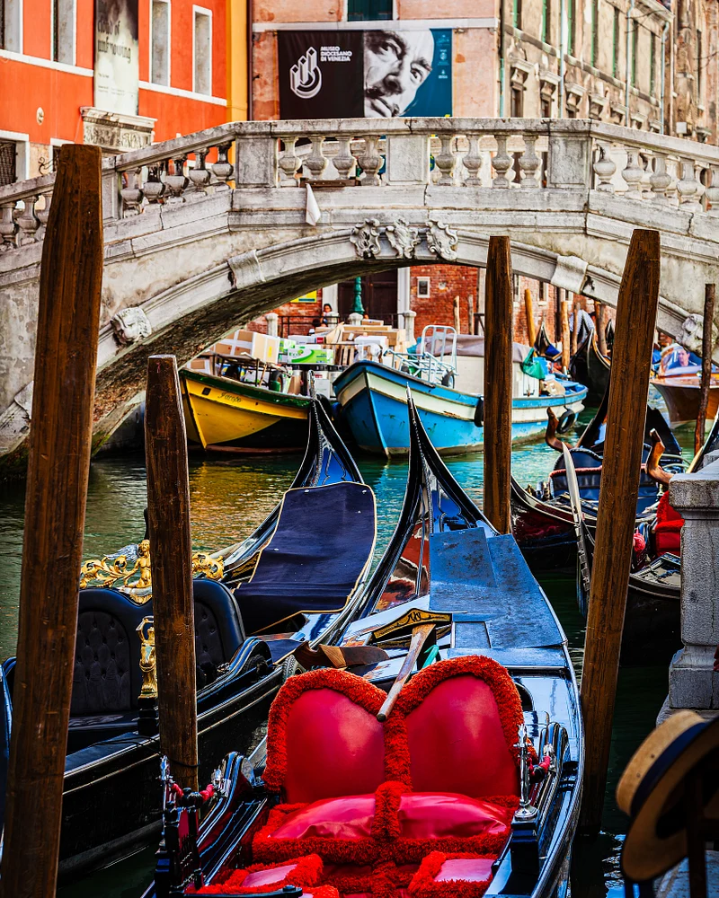 Colorful gondolas under a bridge in Venice, Italy, with artistic mural.
