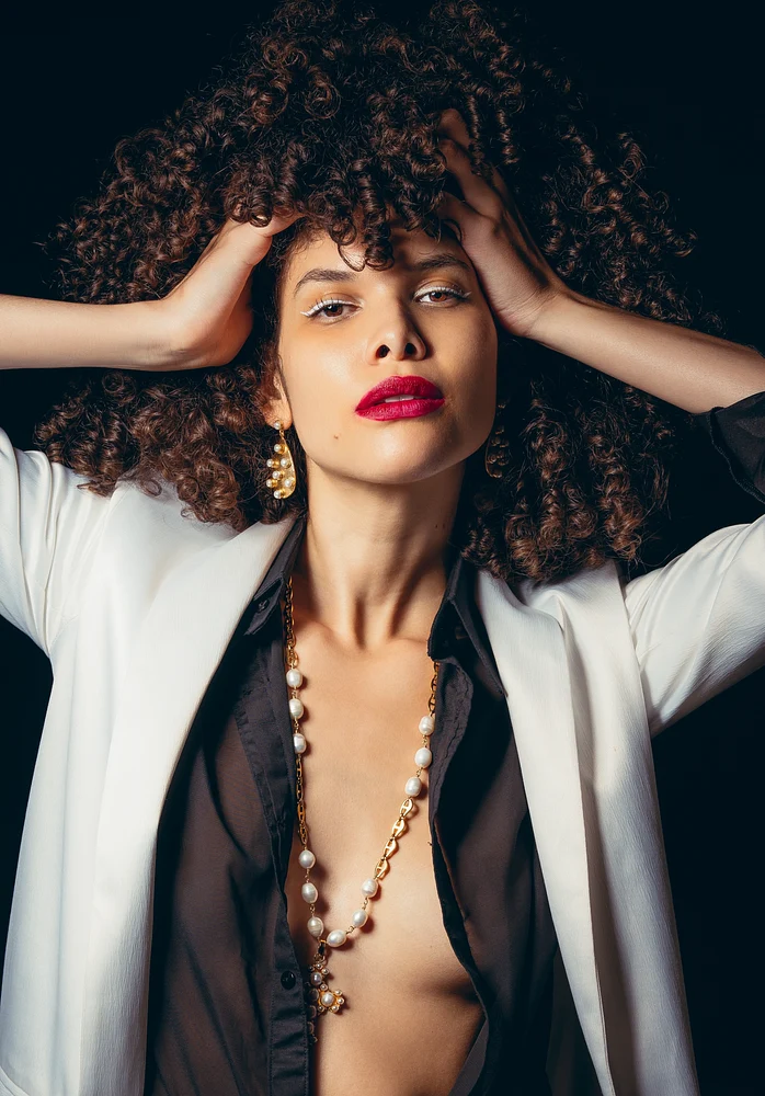 Fashion portrait of a model with curly hair, bold red lips, and elegant jewelry against a dark background.