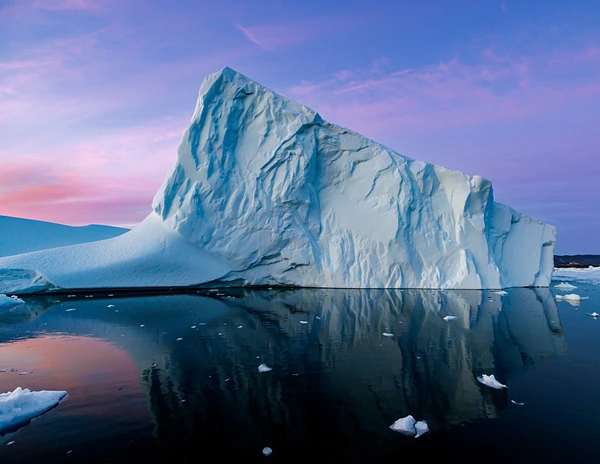 A towering iceberg reflecting vibrant sunset colors in calm waters.