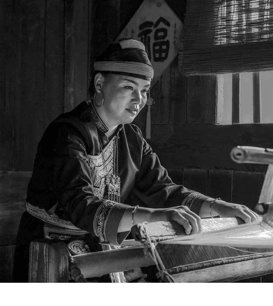 'A She ethnic minority woman, identified by her headdress and attire, carryon with the traditional handicraft of weaving on a lo
